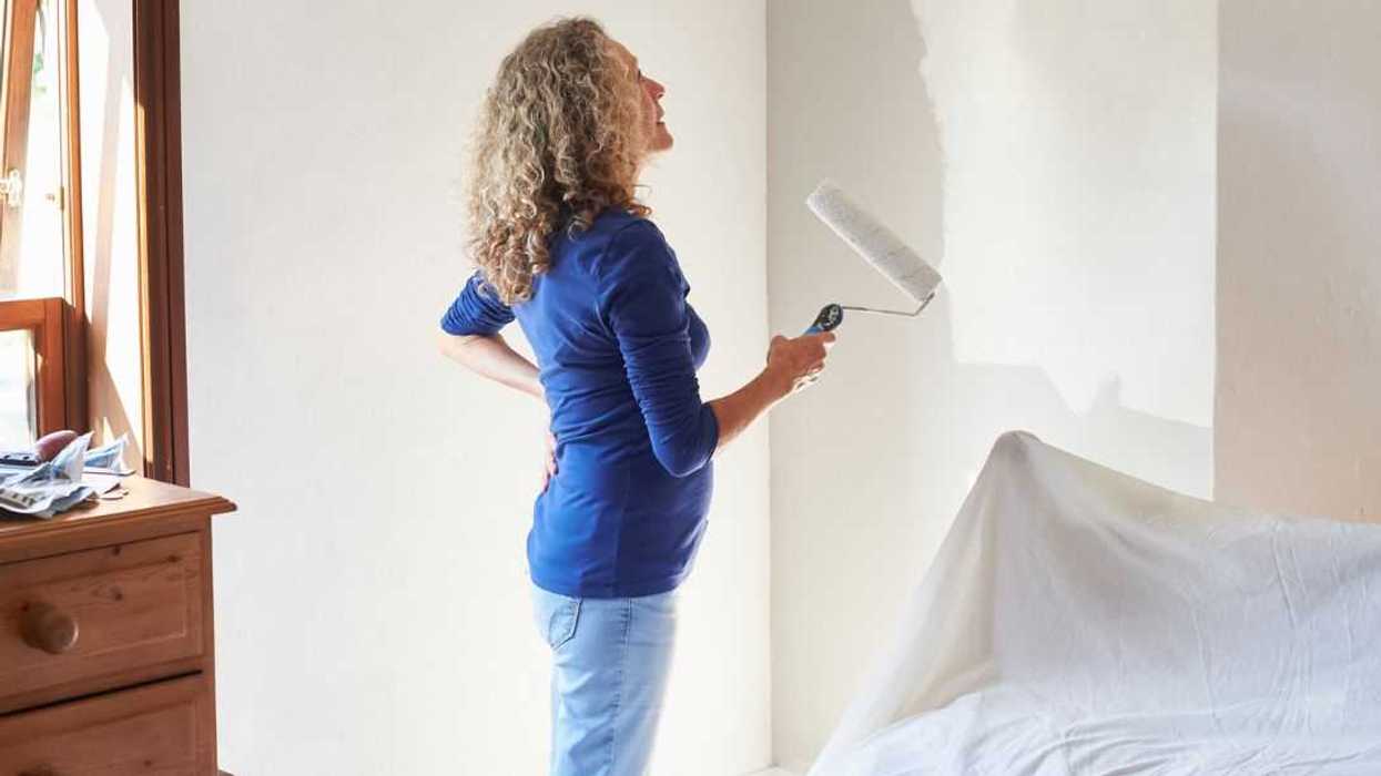 A mature woman painting her bedroom white.