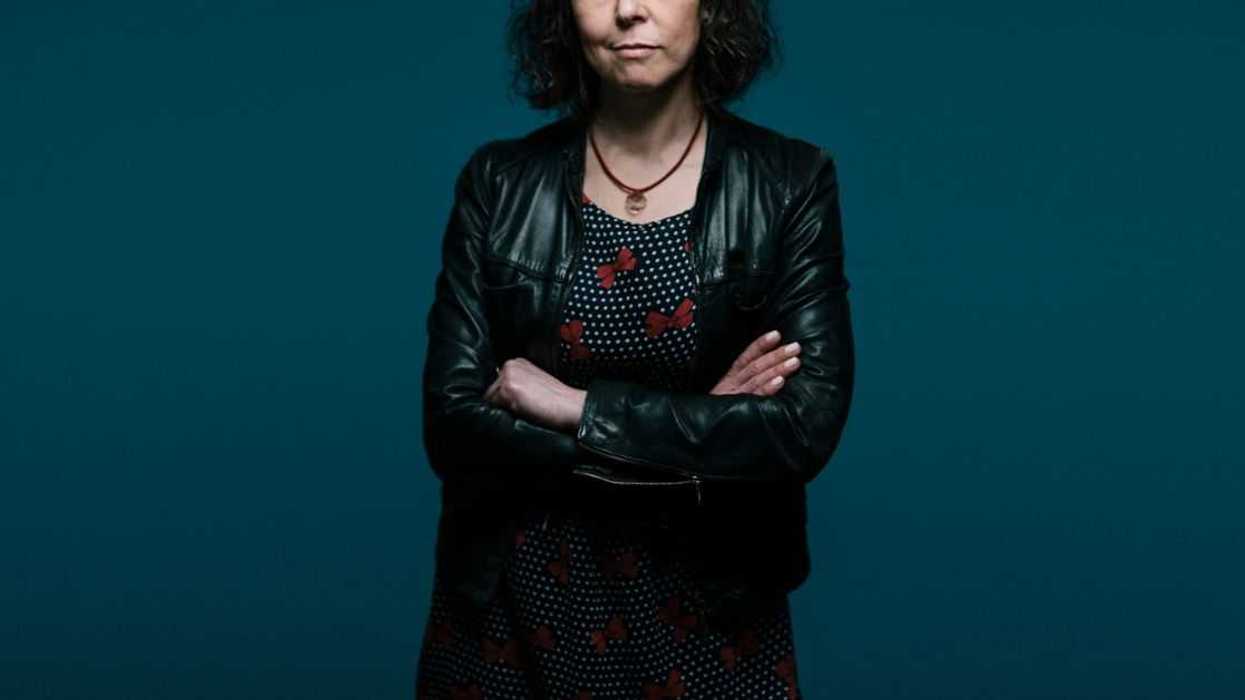 A middle aged woman stands with her arms crossed