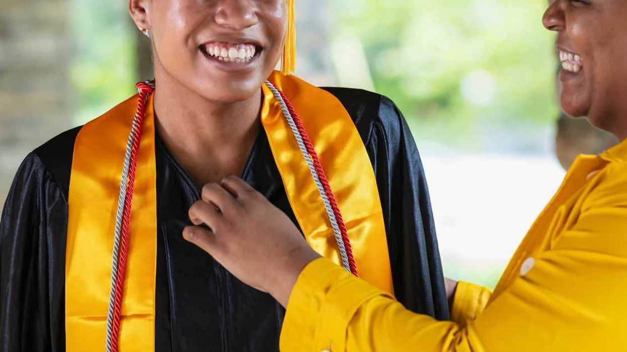 A mother adjusting her daughter's graduation gown.