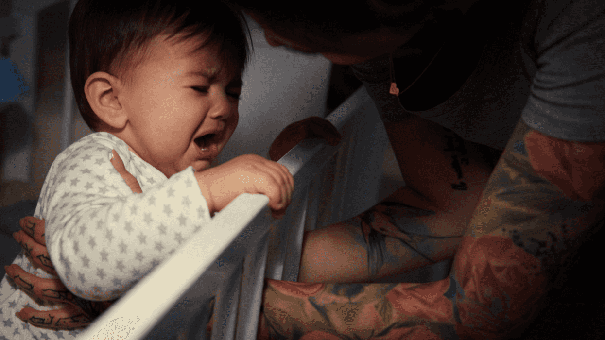 A mother tending to a crying baby in a crib.