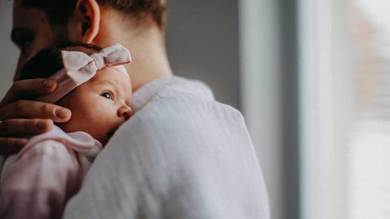 A newborn is held by her father as they stand in front of a window.