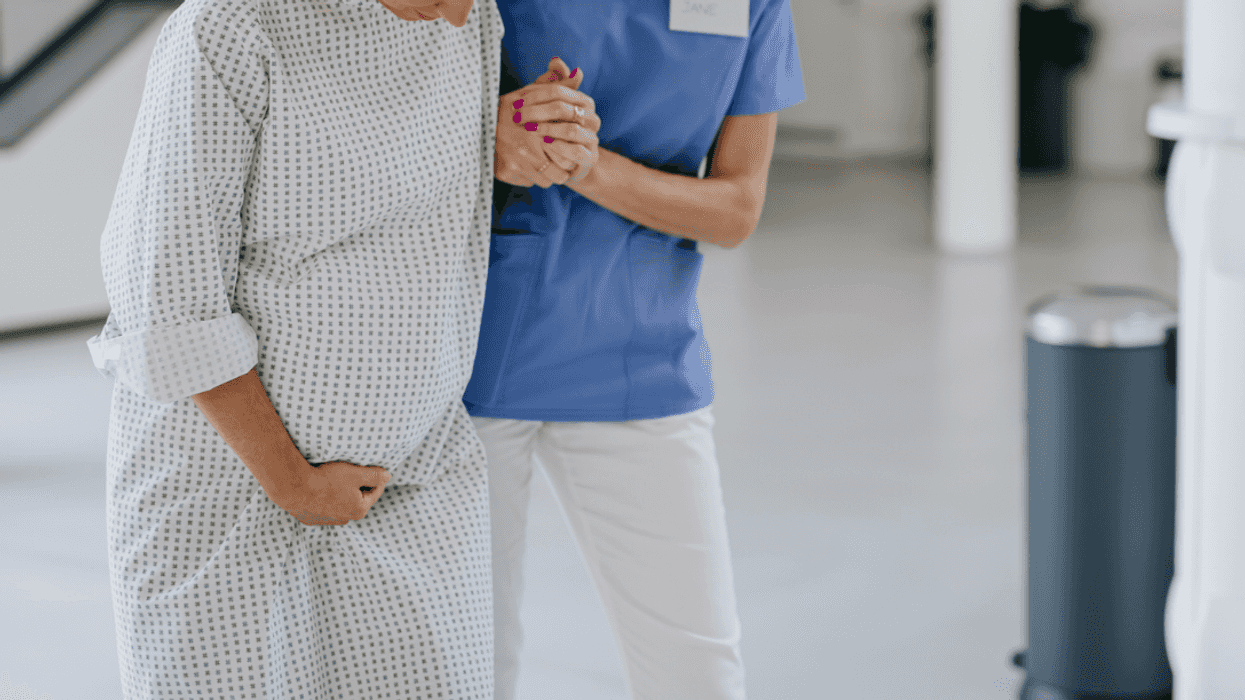 A nurse helping a pregnant woman in a hospital gown walking.