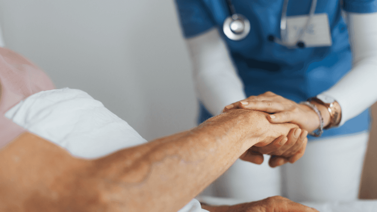 A nurse holding the hand of an older man.