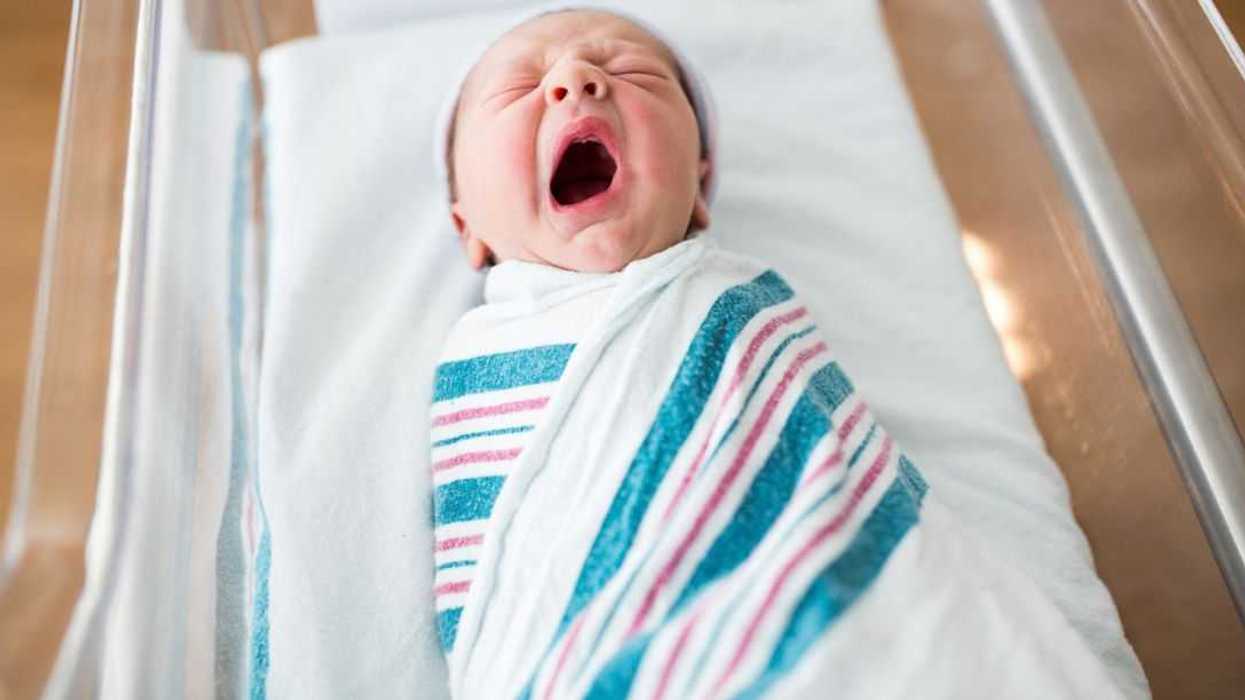 A one-day-old newborn infant yawns in its crib in the hospital.