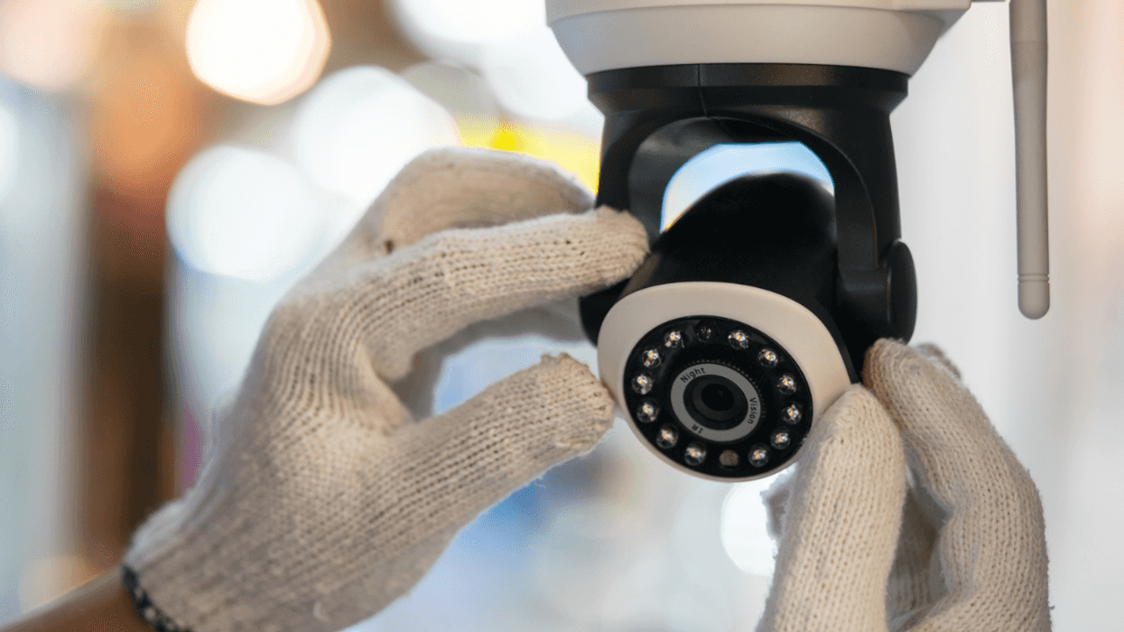 A pair of hands wearing white gloves adjusting a security camera.