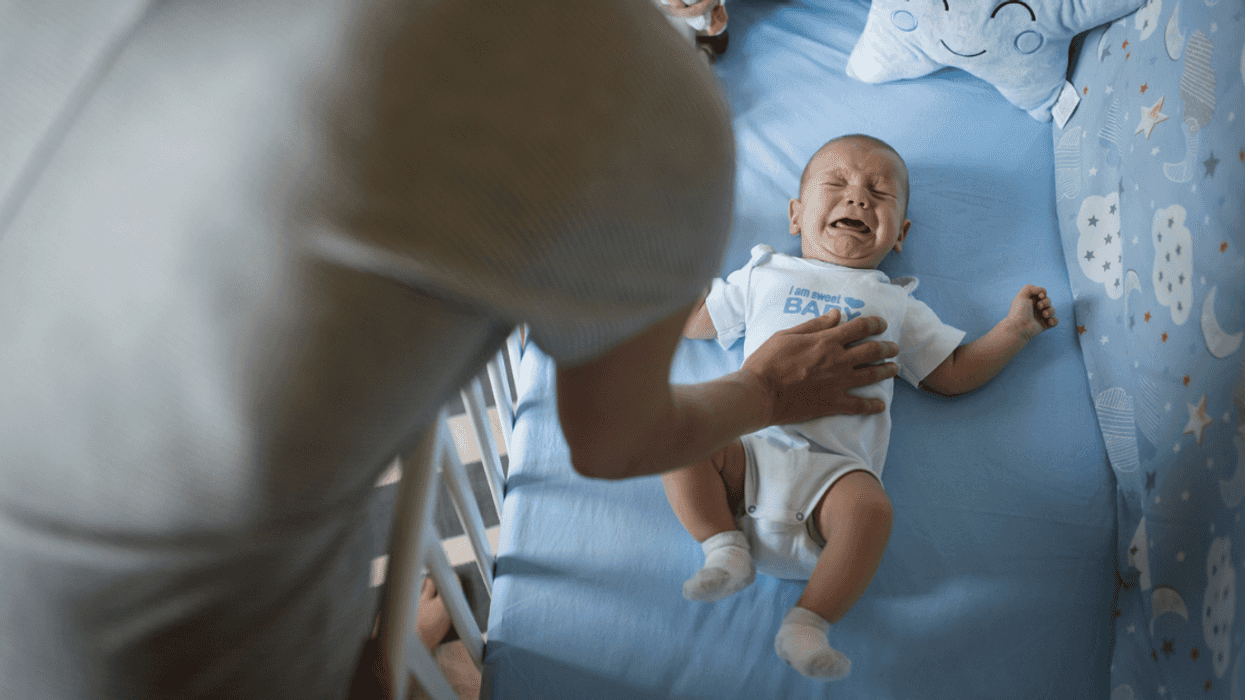 A parent leaning into a crib trying to comfort a crying baby.