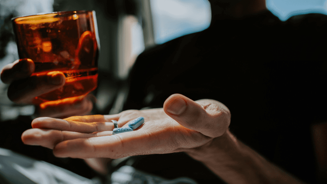 A person holding a glass of water in one hand and a pill in another.