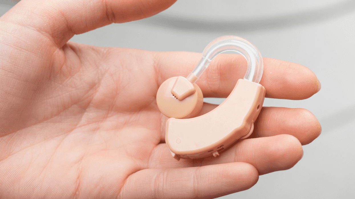 A person holding a hearing aid in their open palm.