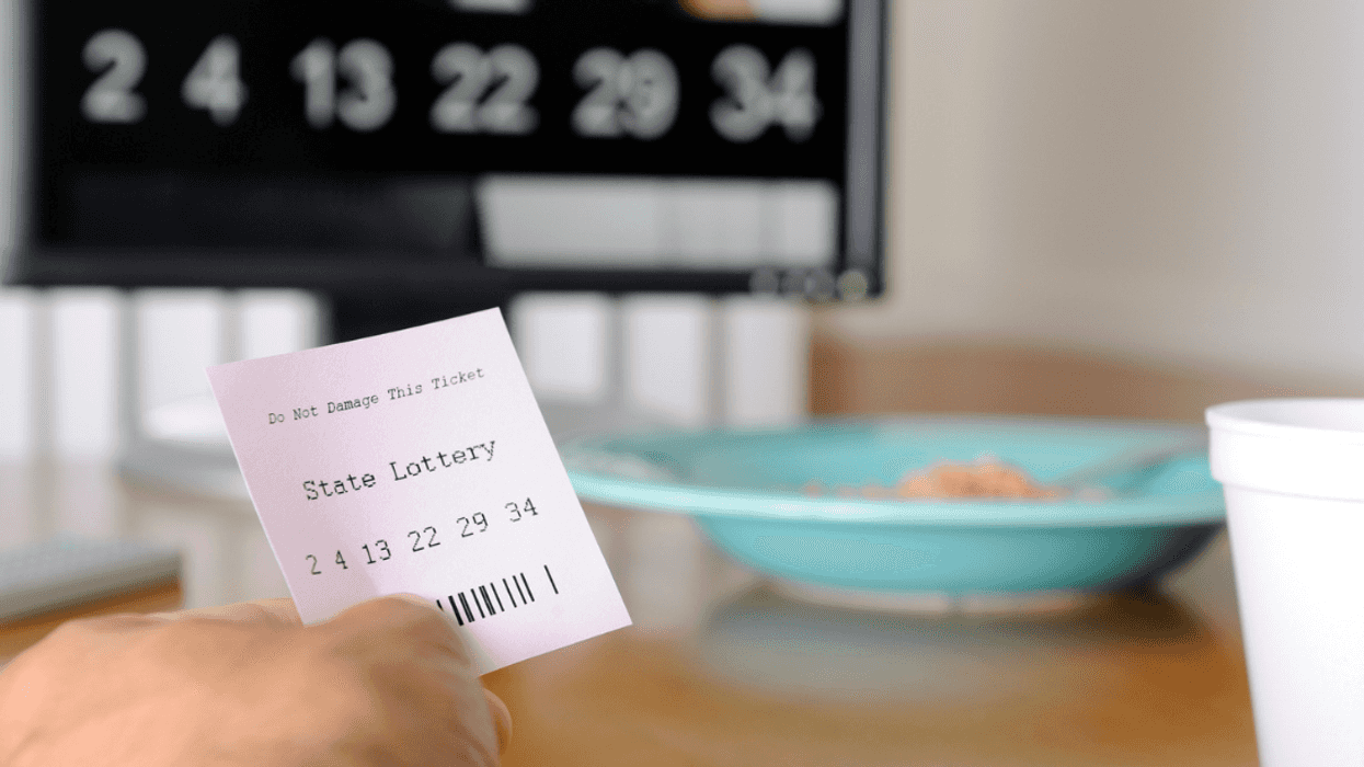 A person holding a lottery ticket with the winning numbers in the background