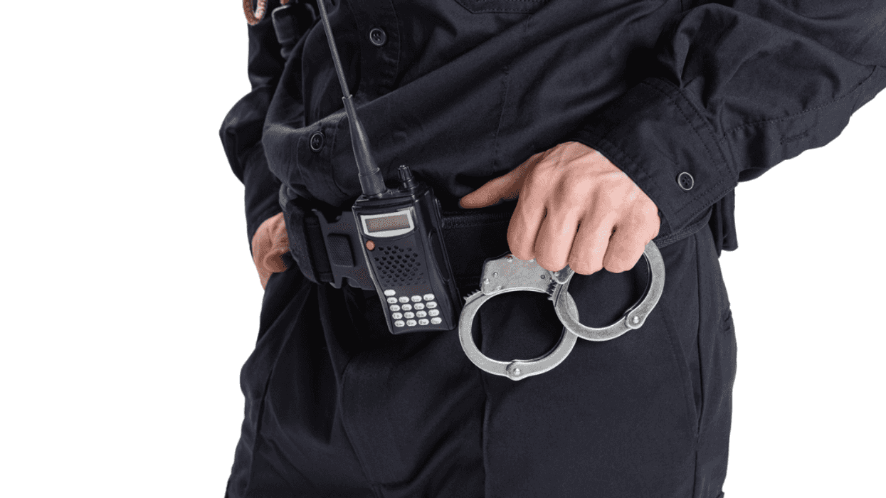 A person in a dark uniform with handcuffs and a walkie talkie on their belt.