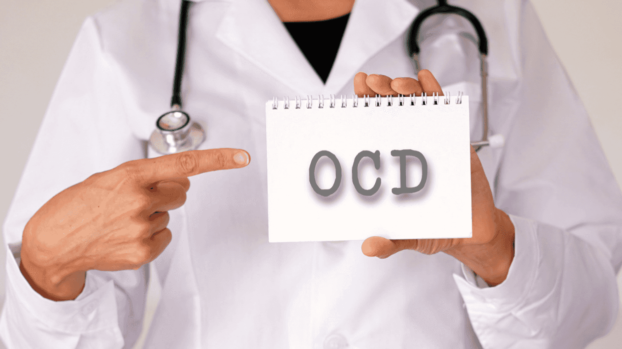 A person in a lab coat with a stethoscope around their shoulders holding a card that says OCD on it.