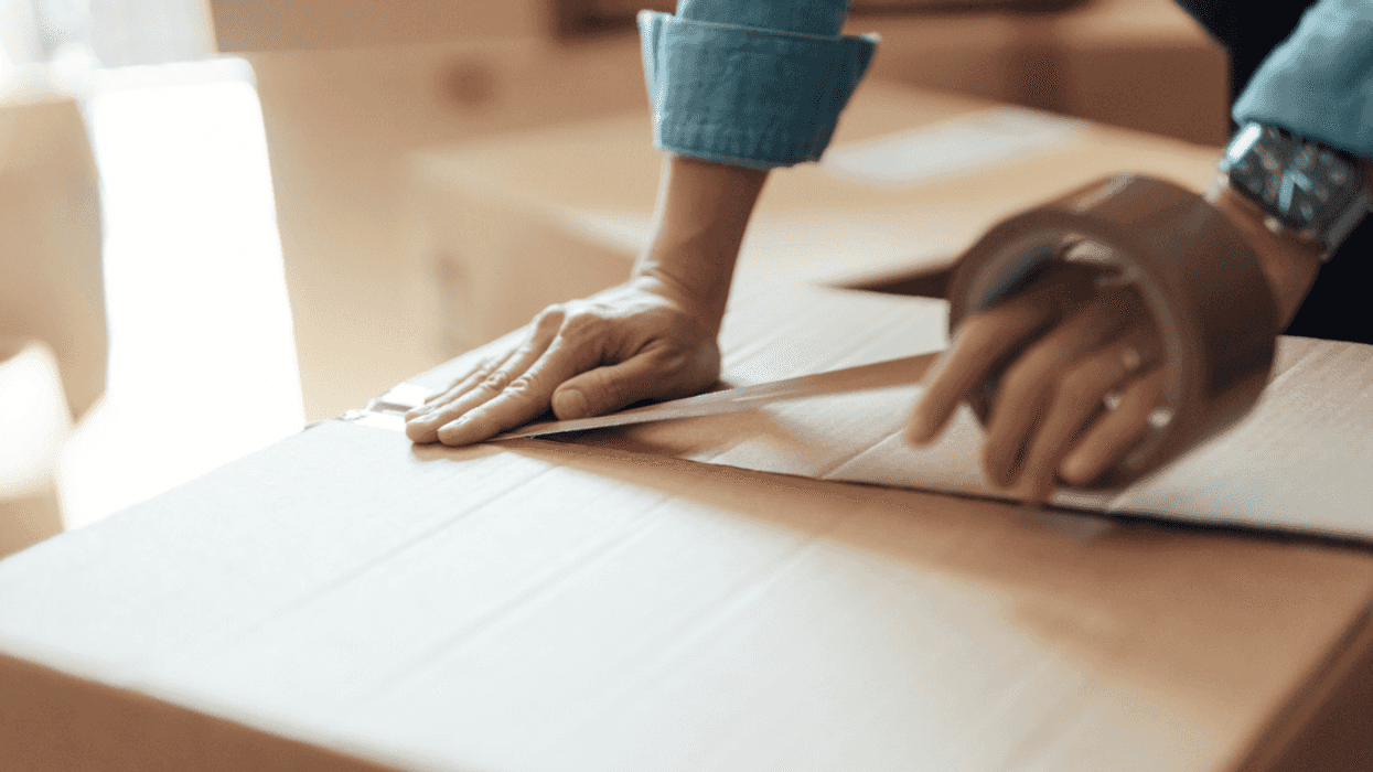A person putting tape on a moving box.