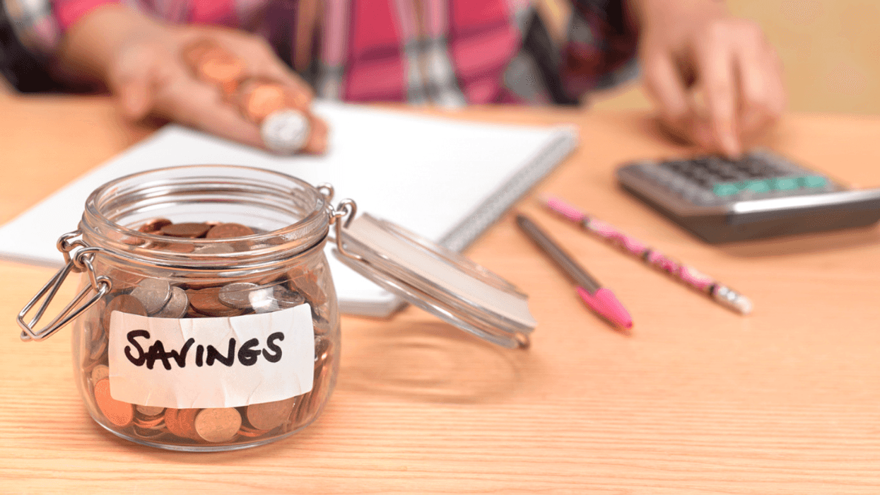 A person sitting at a table with a jar full of change in front of them.