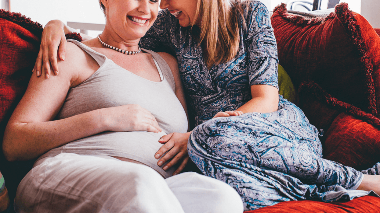 A pregnant woman cuddling with another woman on the sofa.