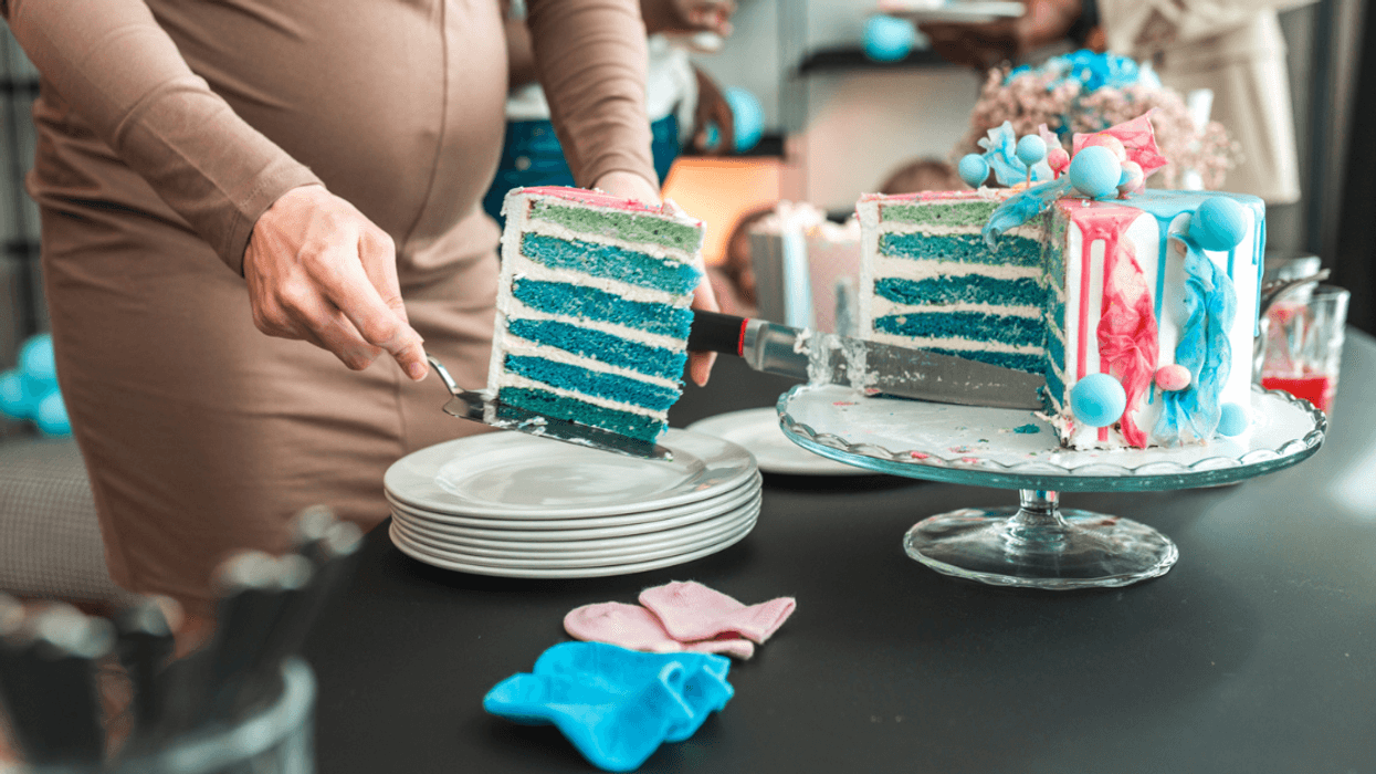 A pregnant woman cutting into a blue gender reveal cake.