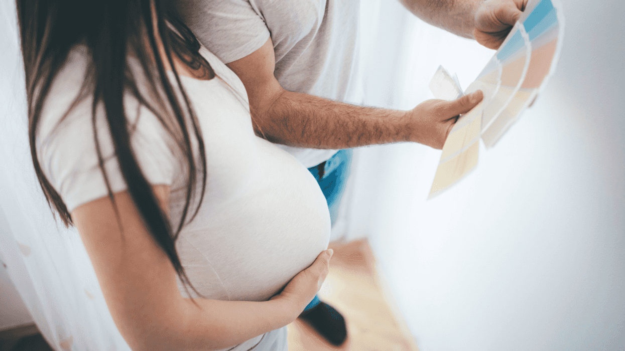 A pregnant woman holding her tummy and looking at paint samples.