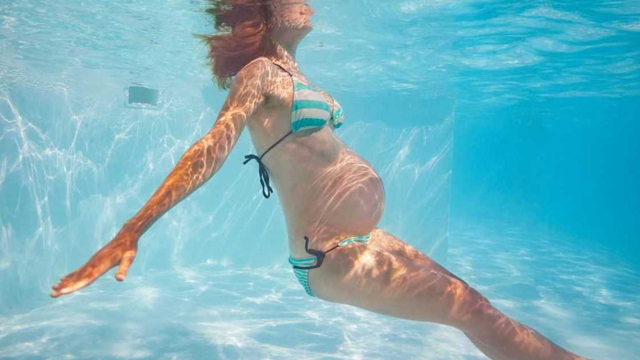 A pregnant woman in a bikini swims underwater