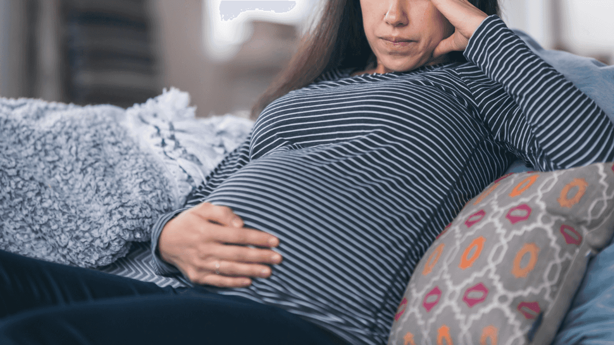 A pregnant woman lying on the sofa with one hand on her stomach, and one hand holding her head.