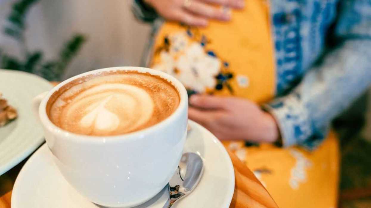 A pregnant woman sits at a table with a coffee drink