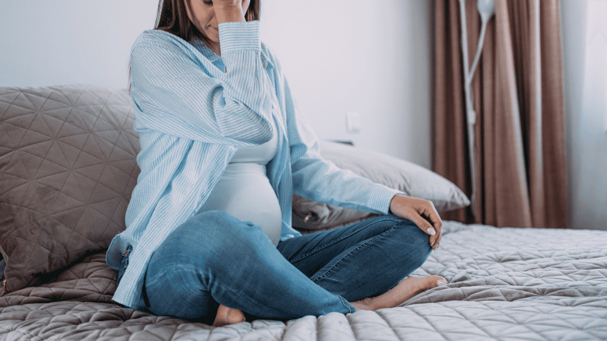 A pregnant woman sitting on a bed, resting her head in her hands.