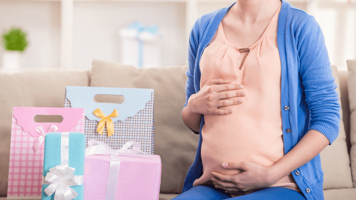 A pregnant woman sitting on a sofa next to a pile of presents.