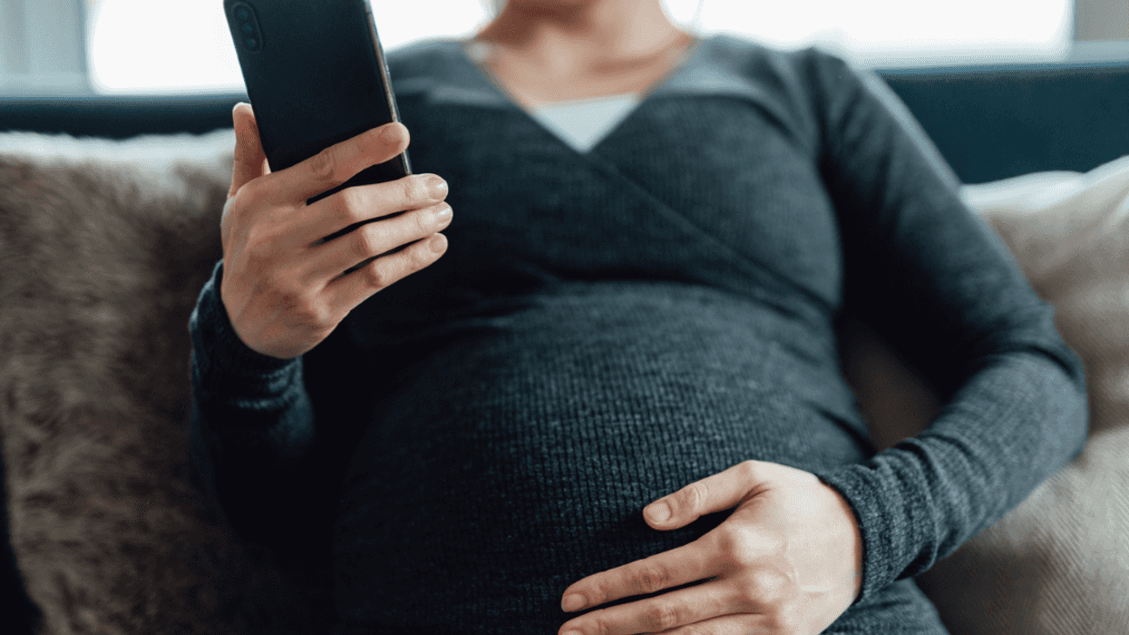 A pregnant woman sitting on the sofa looking at her phone.