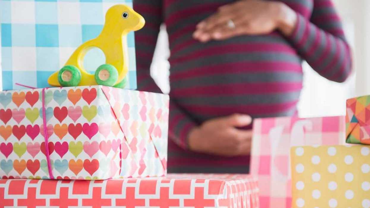 A pregnant woman stands surrounded by gifts at a baby shower