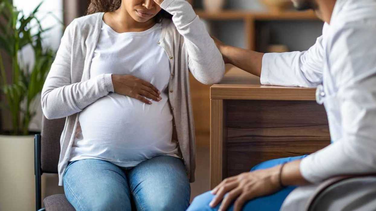 A pregnant young, woman feeling bad, sitting in a chair at a clinic, touching her big tummy and head, visiting doctor, gynecologist comforting crying expecting lady.