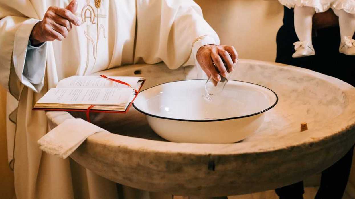 A priest pours the sacred water into the baptismal font during a baby's baptism