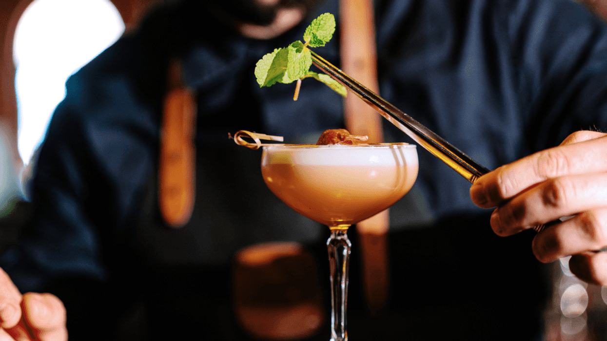 A putting a leafy garnish over a frothy cocktail.