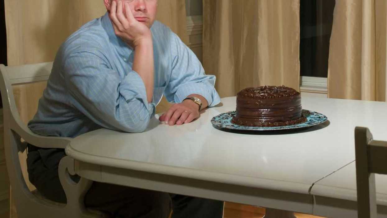 A sad man sits at a table with a chocolate cake