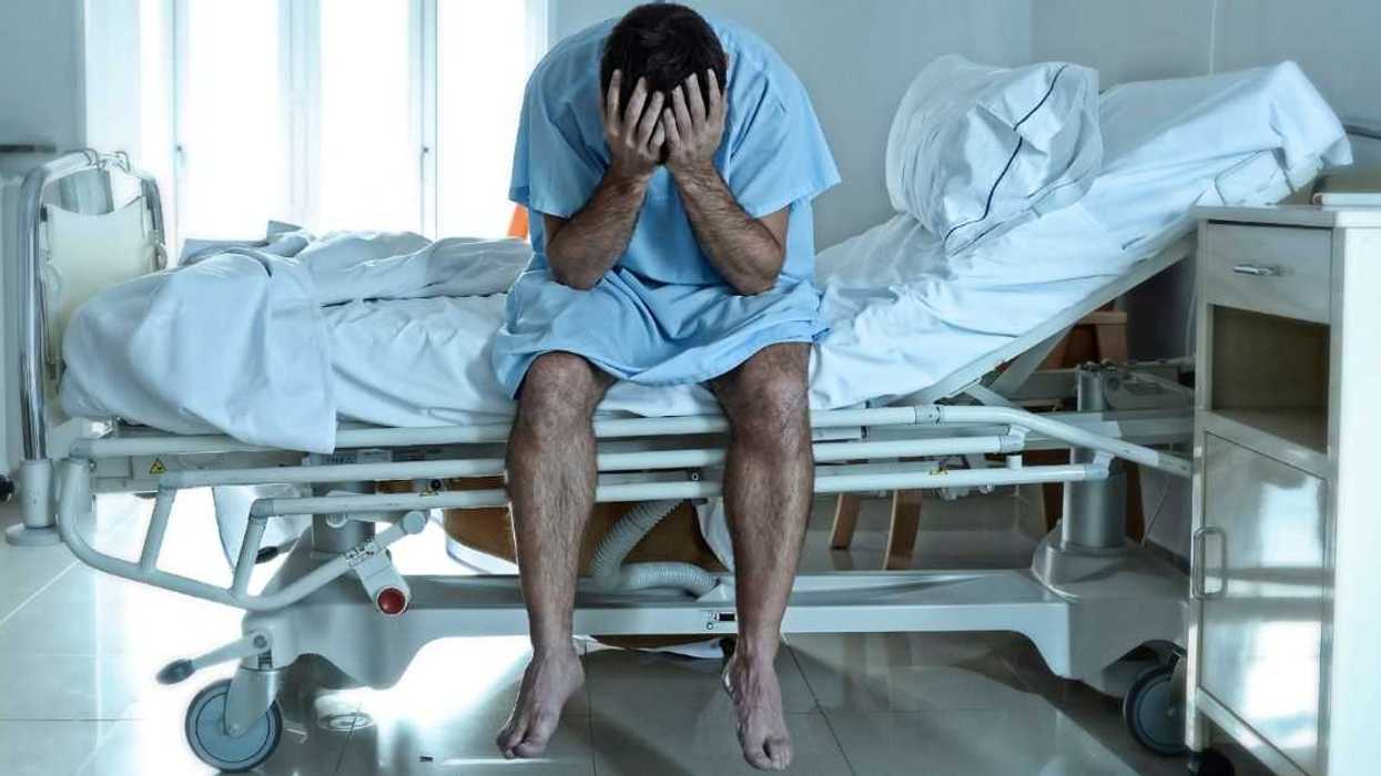 A sad, sick man sits on a hospital bed alone and depressed.