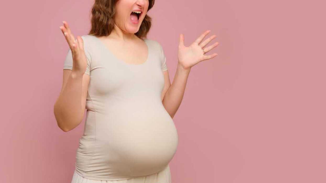 A screaming pregnant woman on a studio pink background.