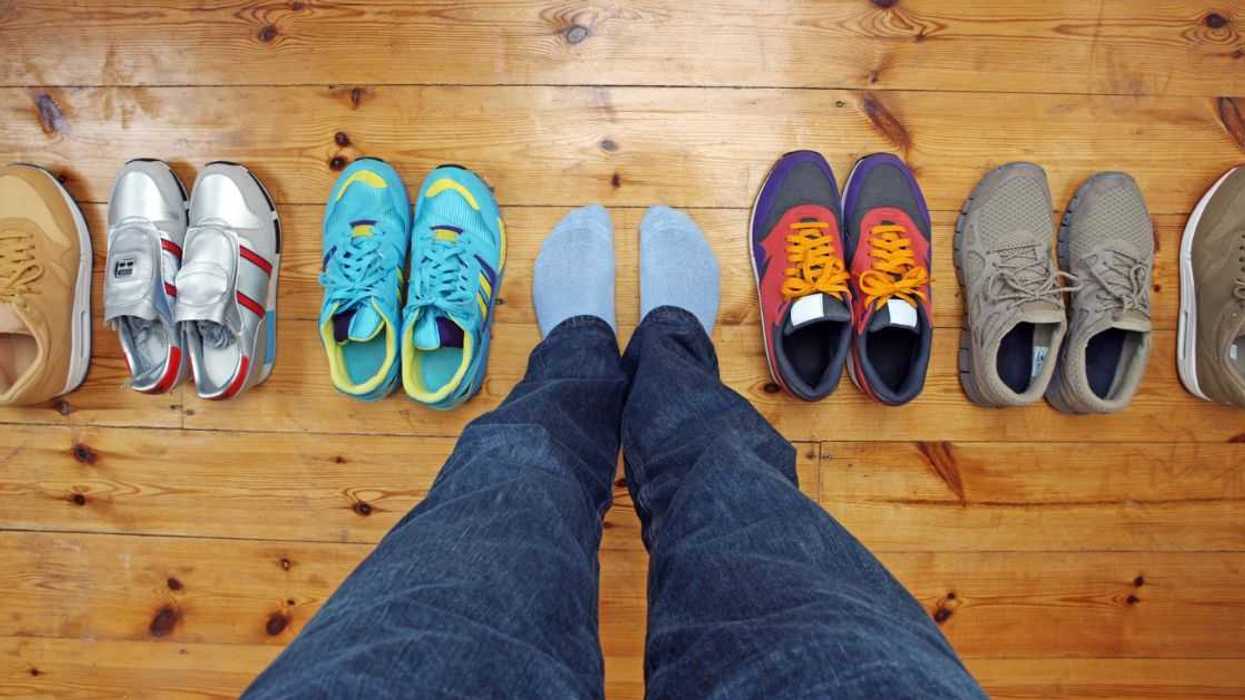 A shot of a person's feet surrounded by shoes on a wooden floor.