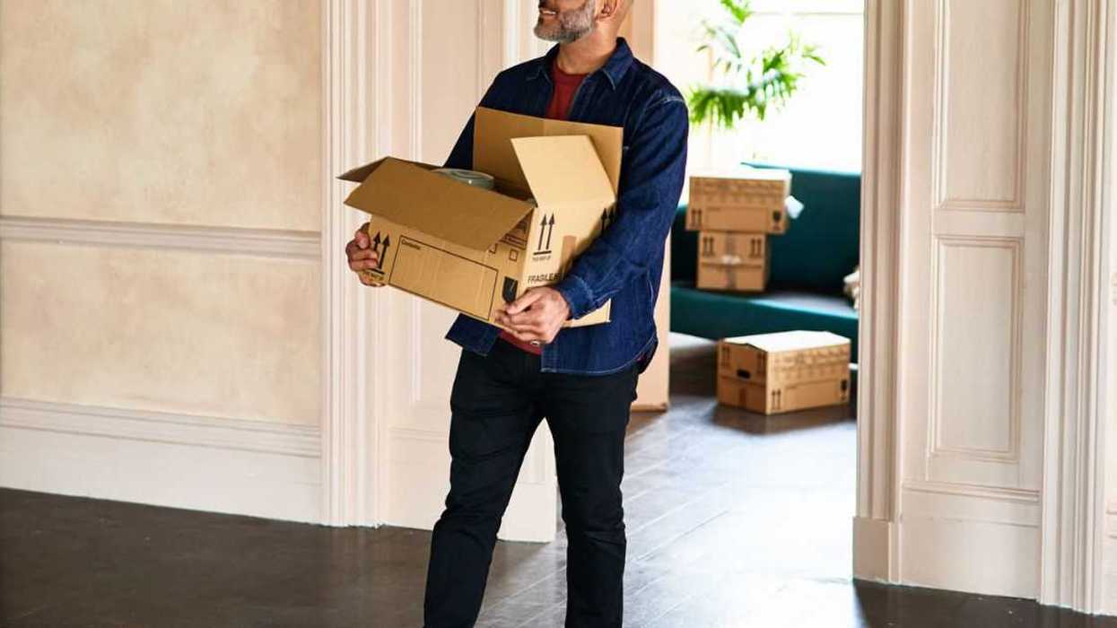 A smiling, mature man walking into empty room of new home, carrying a cardboard box and looking around happily. Excitement, new home, moving, house.