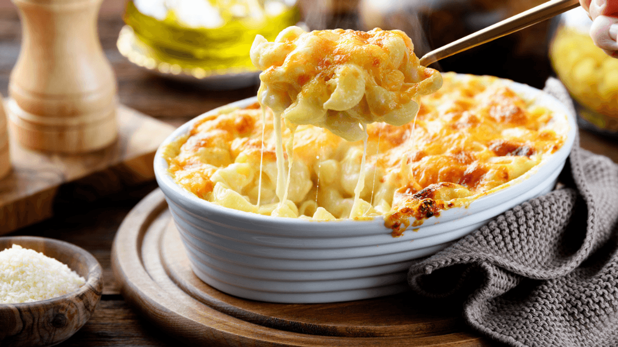 A spoon pulling out a serving of macaroni and cheese from a bowl.