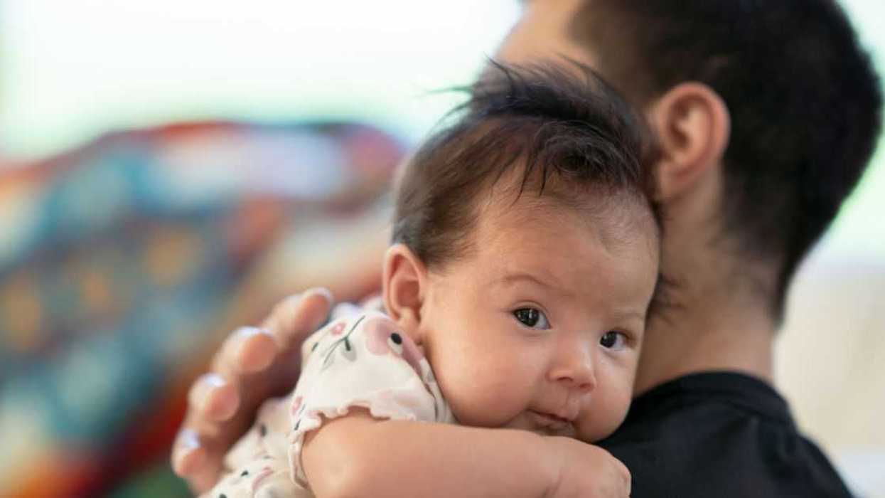 A sweet little newborn looks at the camera as she is propped up on her father's shoulder.
