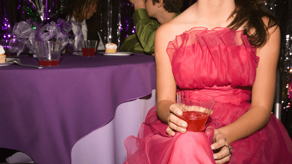 A teen girl in a pink prom dress sitting down and holding a drink.