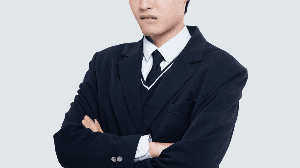 A teenage boy in a coat and tie crossing his arms.