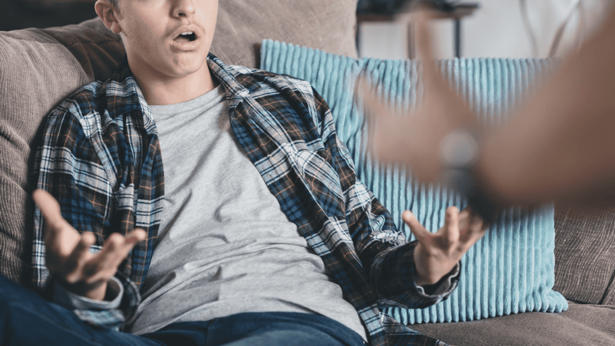 A teenage boy sitting on the couch holding out his arms and hands.