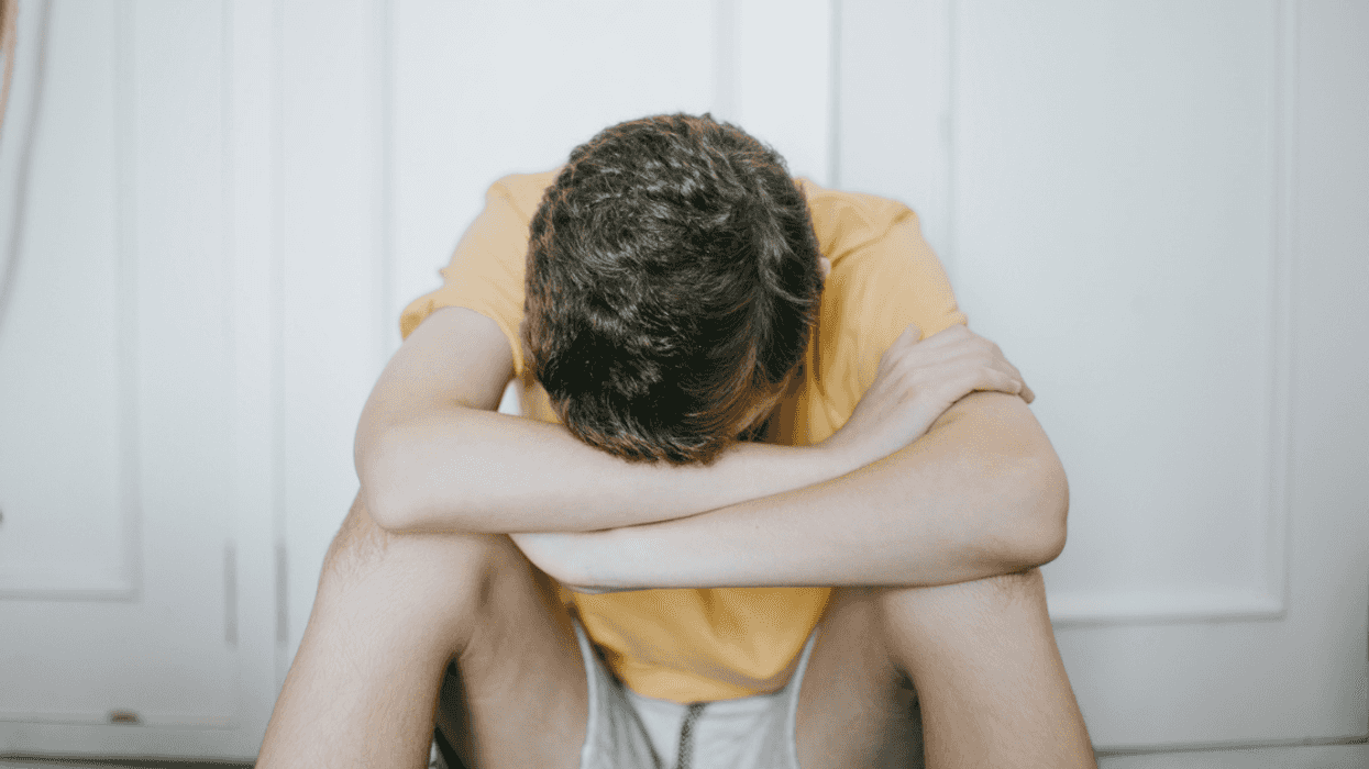 A teenage boy sitting on the floor with his head in his hands.