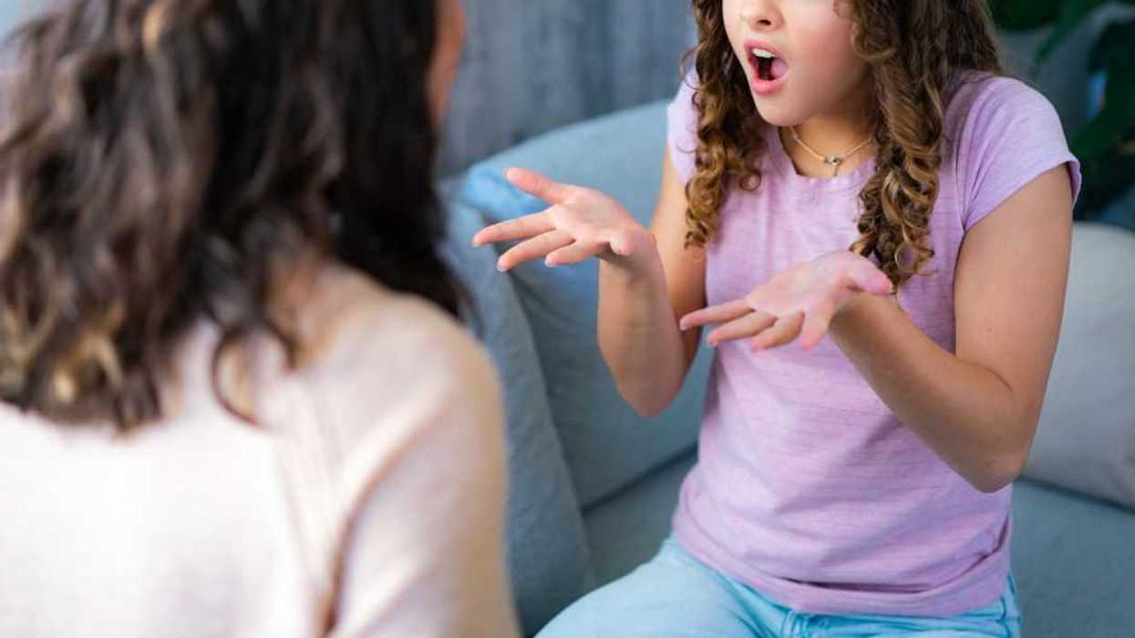 A teenage girl is talking angrily to her mother as they sit on the couch at home.