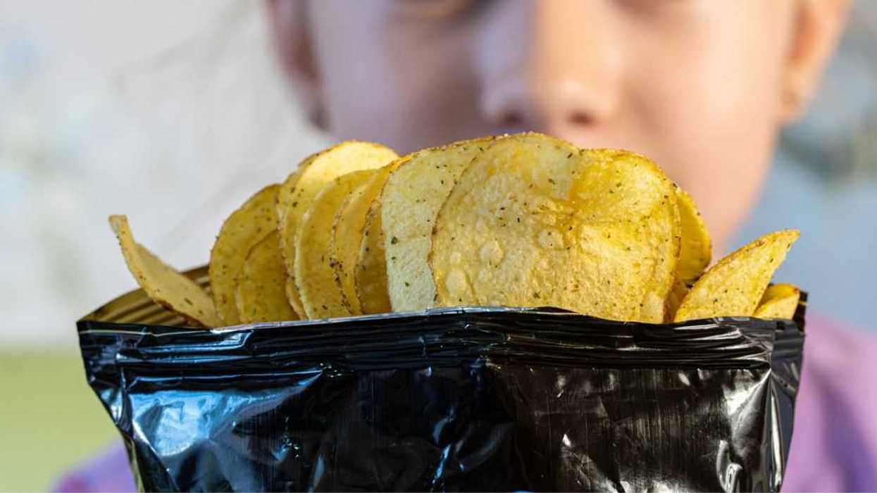 A teenage girl looks with surprise and joy at an open pack of chips.