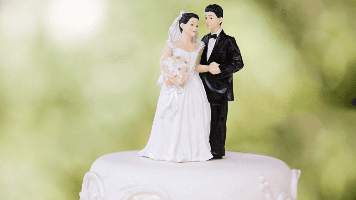 A wedding cake with a bride and groom cake topper on top.