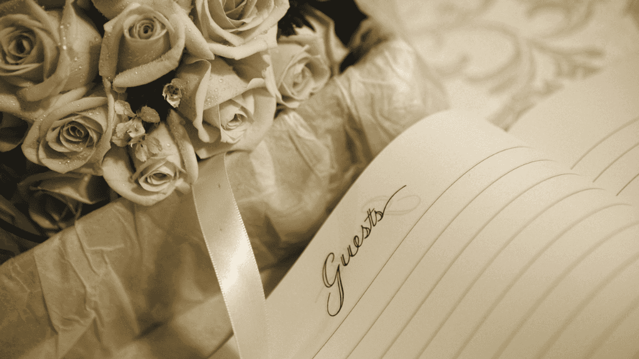 A wedding guest list book lying on a table with roses and ribbon on it.