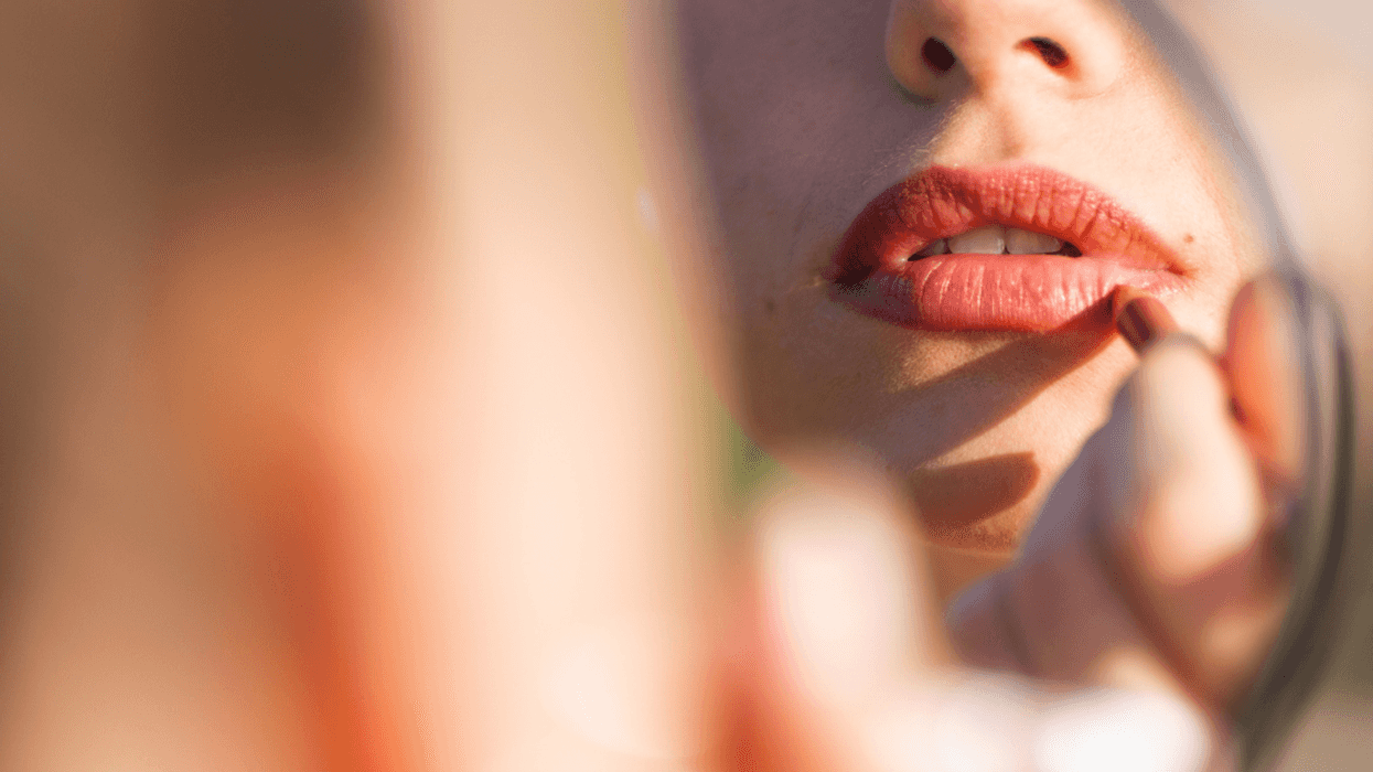 A woman applying red lipstick to her lips.