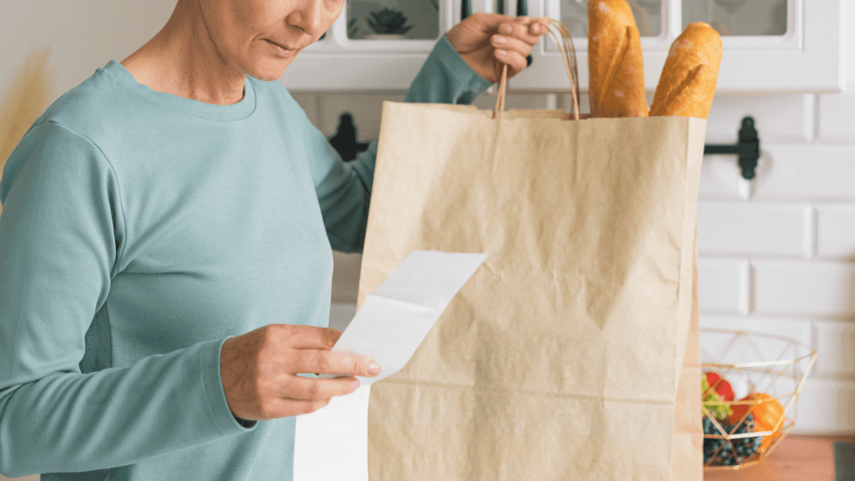 A woman at a counter looking at a list next to a bag full of groceries.