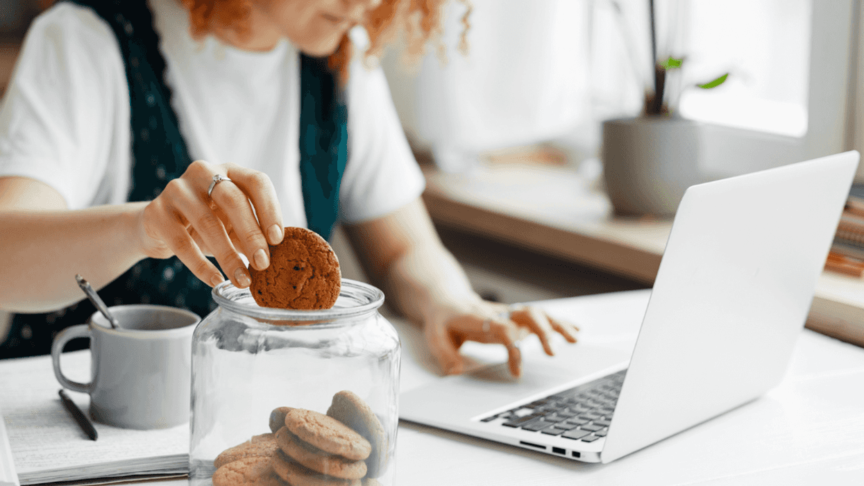 A woman at her computer dipping a cookie into a glass of milk.