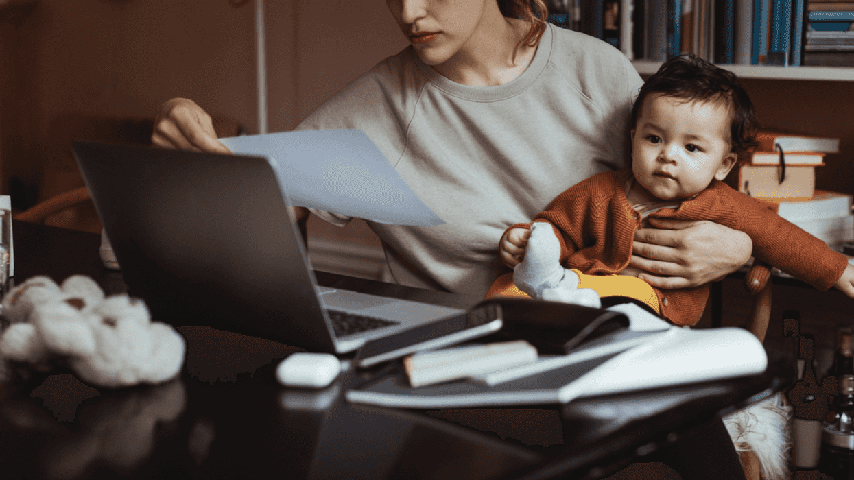 A woman. at her desk with a baby on her lap.