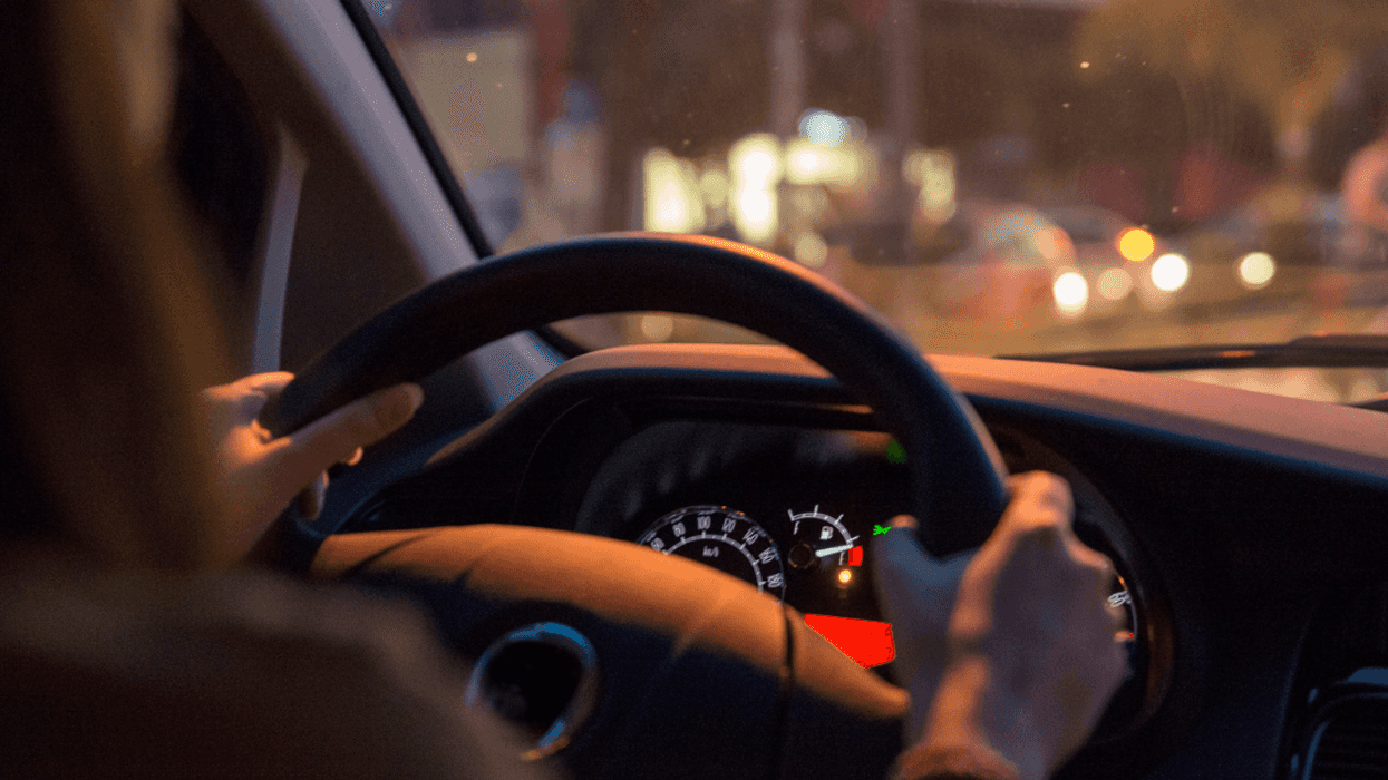 A woman behind the wheel of a car with the. gas gague on empty.